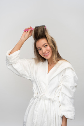 Hermosa joven recogiendo su cabello con un cepillo de pelo redondo