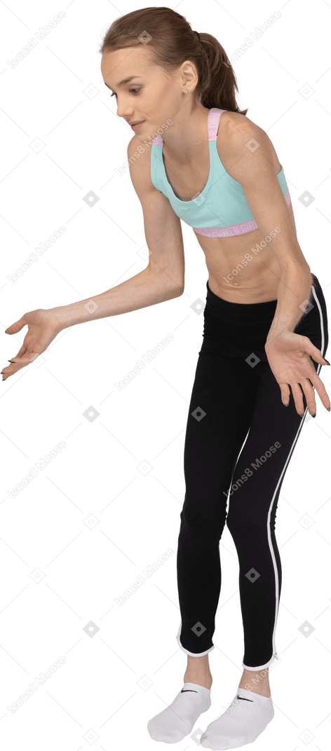 Vista de tres cuartos de una jovencita en ropa deportiva extendiendo las manos y mirando hacia abajo