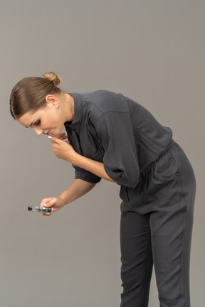 Three-quarter view of a young woman in a jumpsuit holding a magnifying glass