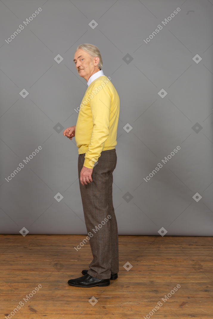 Side view of a thoughtful old man raising hand and looking at camera