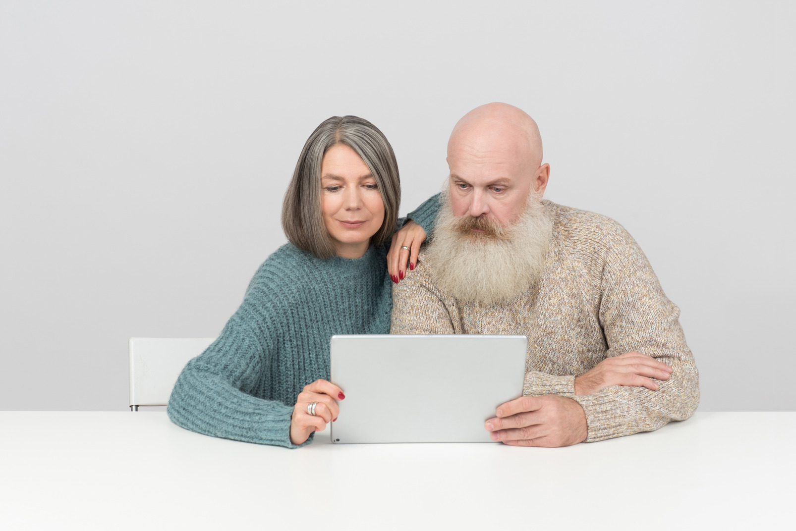 Aged couple sitting at table and looking at digital tablet