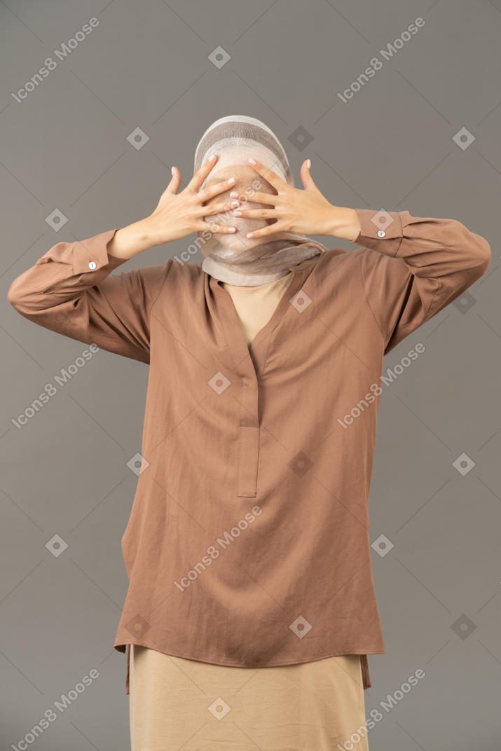 Front view of woman covered with headscarf spreading fingers in front of her face