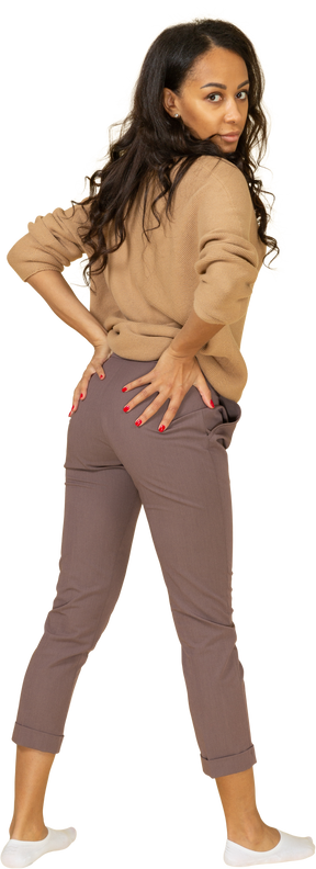 Vista posterior de tres cuartos de una mujer joven de piel oscura poniendo las manos en el trasero