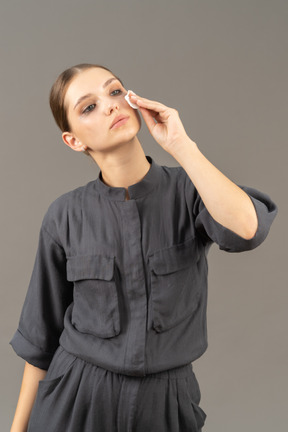 Front view of a young woman in a jumpsuit removing make-up