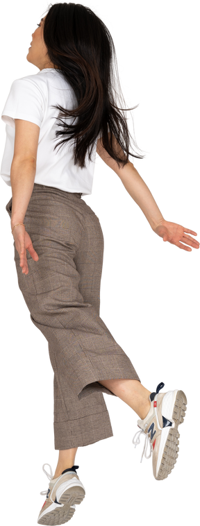 Vista posteriore di tre quarti di una giovane donna che salta in calzoni e maglietta
