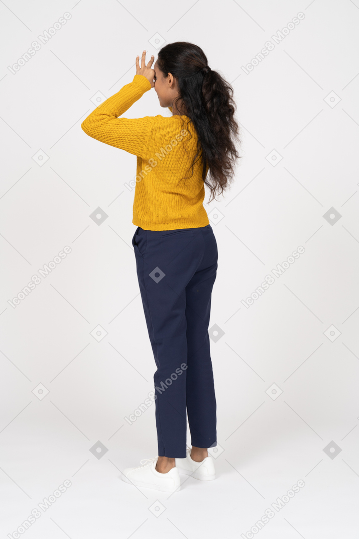 Vista lateral de una niña en ropa casual mirando a través de los dedos
