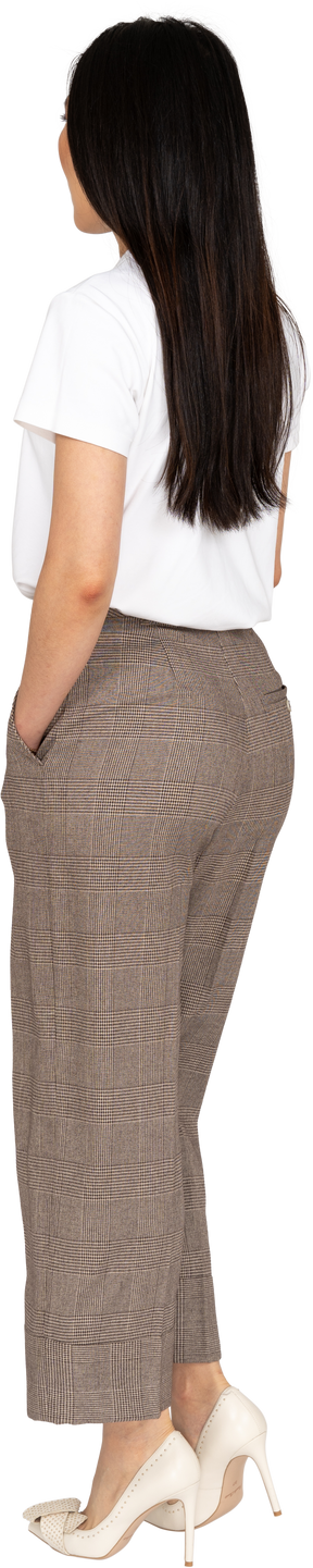 Vista posteriore di tre quarti di una giovane donna seria in calzoni mettendo la mano in tasca