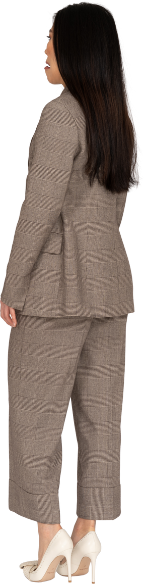 Three-quarter back view of a grimacing young lady in brown business suit