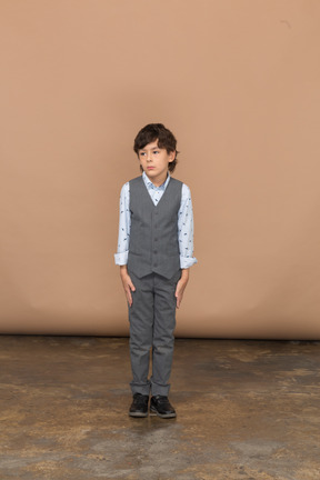Vista frontal de un niño tímido en traje gris parado