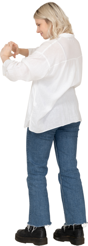 Vista posteriore di tre quarti di una donna bionda in abiti casual che mostra un gesto del cuore