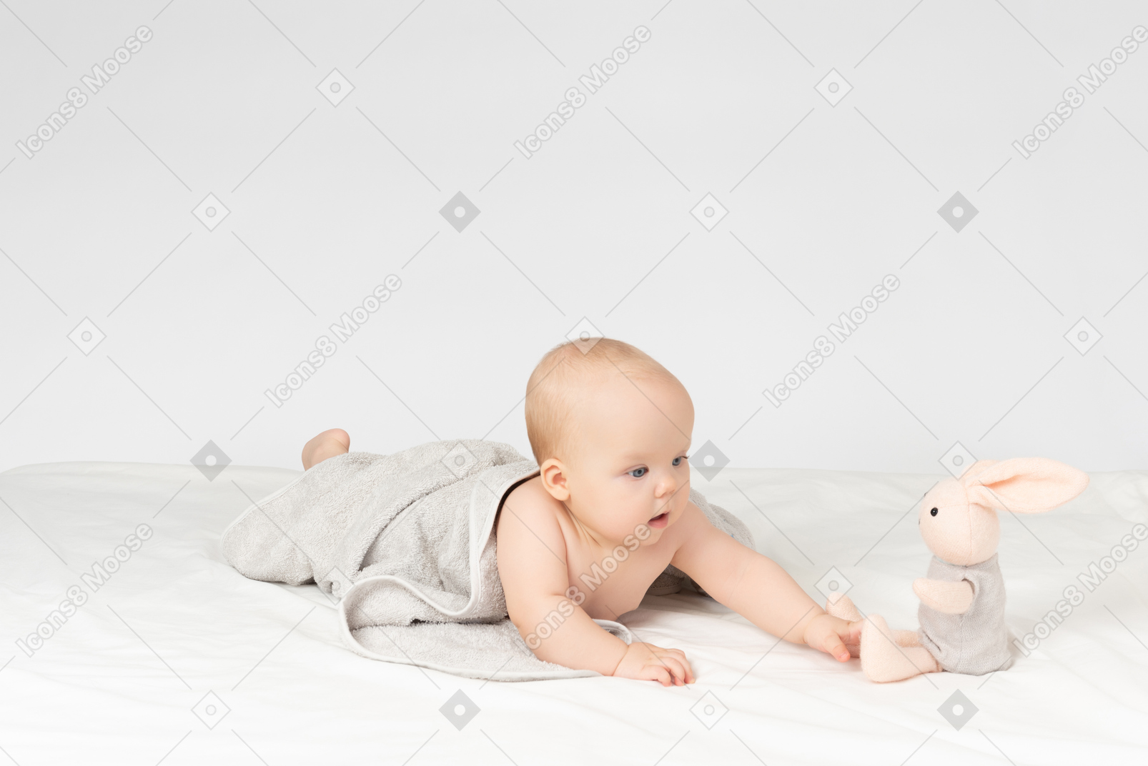 Baby girl covered in towel and looking on stuffed toy