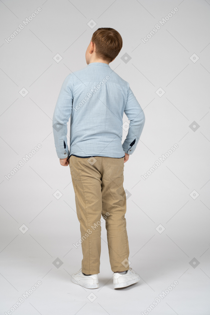 Vista trasera del niño posando con las manos en los bolsillos
