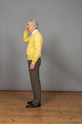 Seitenansicht eines verwirrten alten mannes, der kopf berührt und einen gelben pullover trägt