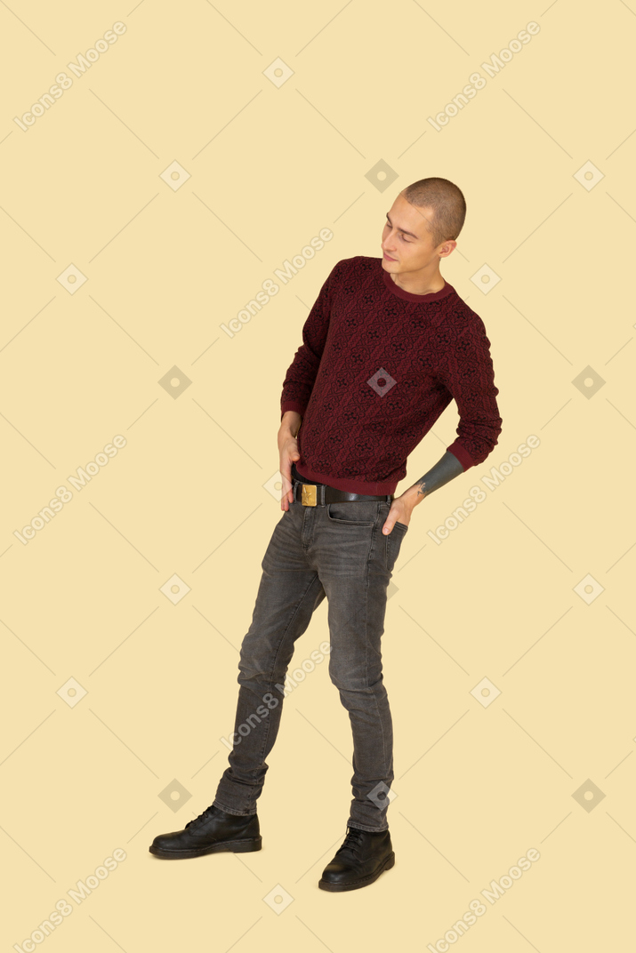 Вид в три четверти идущего молодого человека в красном пуловере, кладущего руку в карман