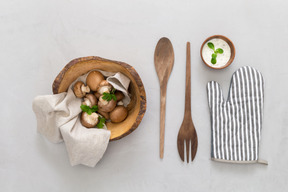 Champiñones en cuenco de madera, cubiertos de madera, especias y guante de horno.