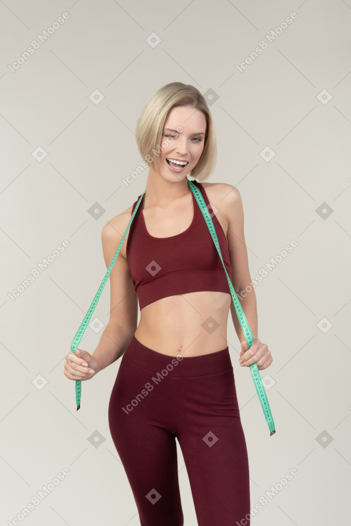 Кокетливая молодая женщина в спортивной одежде держит правую ленту над шеей
