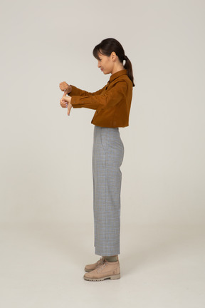 Вид сбоку молодой азиатской женщины в бриджах и блузке показывает палец вниз