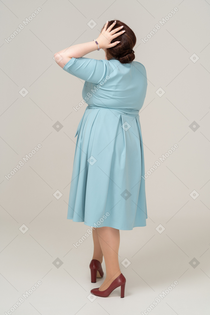 頭に手を置いてポーズをとって青いドレスを着た女性の背面図