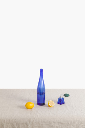 Botella azul, spray de perfume y limones sobre un mantel de lona