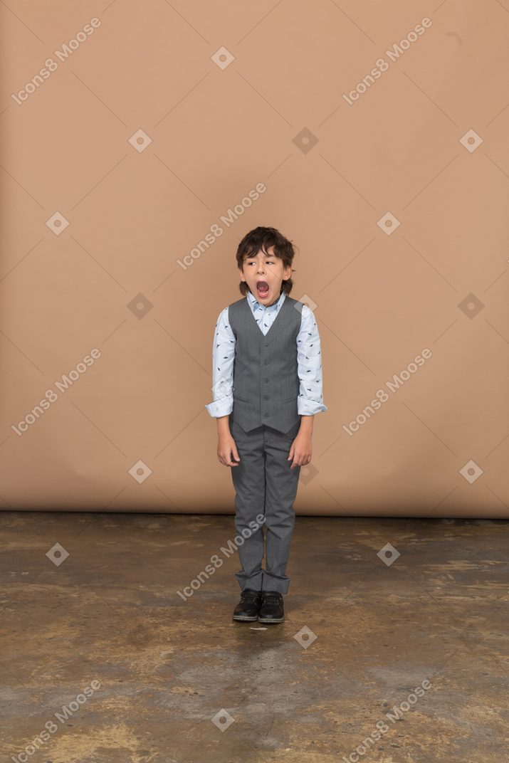 Vue de face d'un garçon en costume regardant la caméra et bâillant