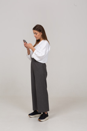 Three-quarter view of a young lady in office clothing checking feed via phone