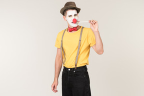 Male clown facing the camera and biting lollipop