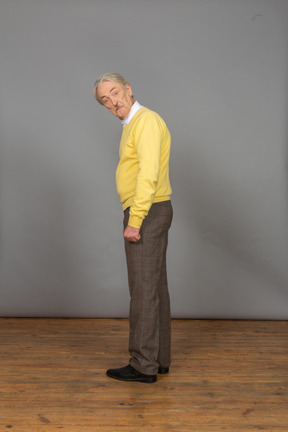 Vista laterale di un uomo anziano sorpreso in pullover giallo chinandosi e guardando la fotocamera