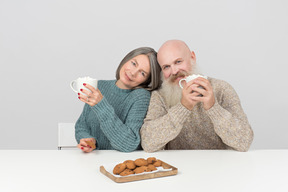 Aged couple holding cups and sitting side to side