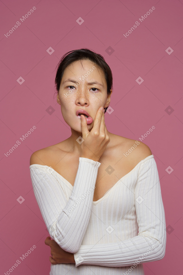 Front view of a perplexed female touching her lips and looking at camera