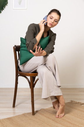 Vue de face d'une jeune femme assise sur une chaise tout en ayant un appel téléphonique