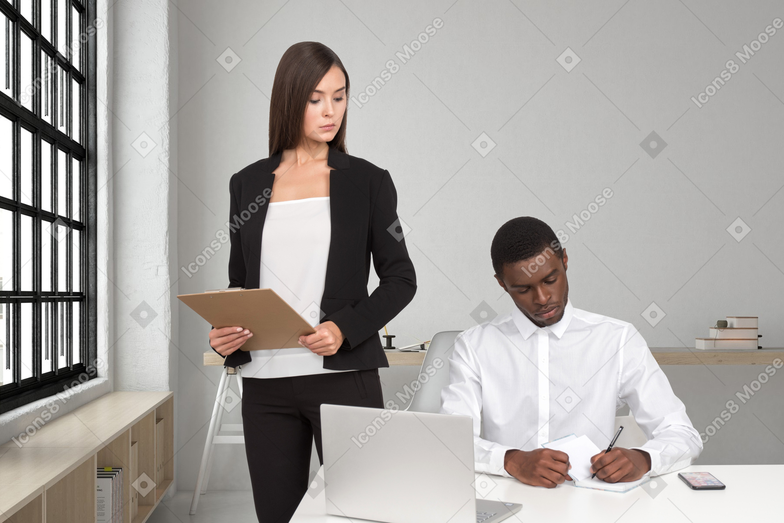 A woman in a business suit standing next to a man working on a laptop
