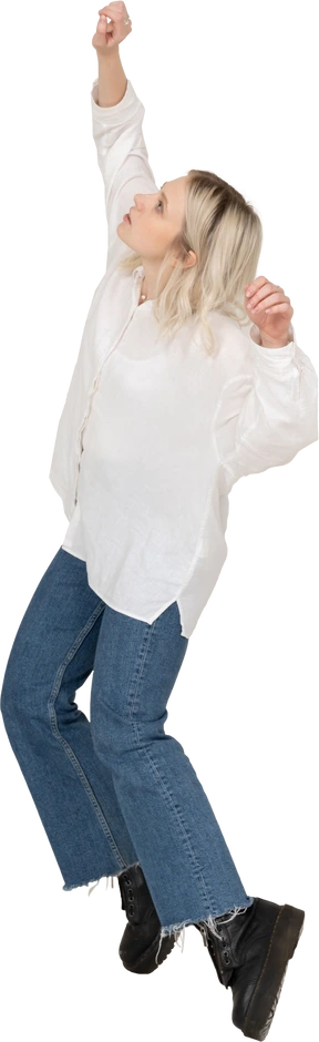 Three-quarter view of a blonde female in casual clothes dancing on her tiptoes and raising hands and head
