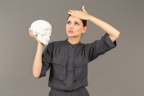 Front view of a young woman in a jumpsuit holding a plaster skull