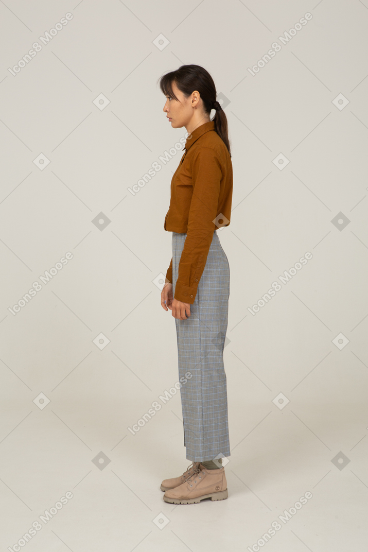 一位身着马裤和衬衫的年轻亚洲女性站着不动的侧视图
