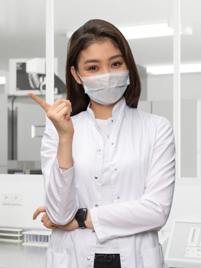 A woman in lab coat with face mask standing in a lab