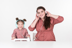 Mother and her little daughter, dressed in red and pink clothes, sitting at the dinner table, listening to the music together