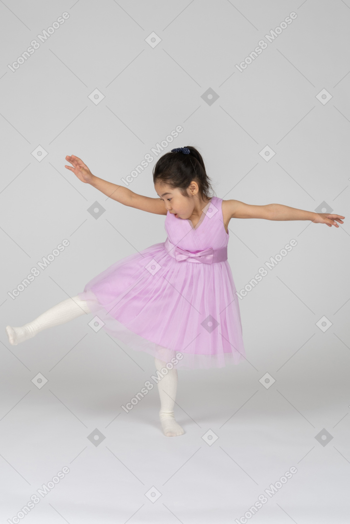 Ragazza in un vestito rosa in piedi su una gamba con le mani aperte