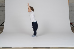 Side view of a little boy standing with his arms raised