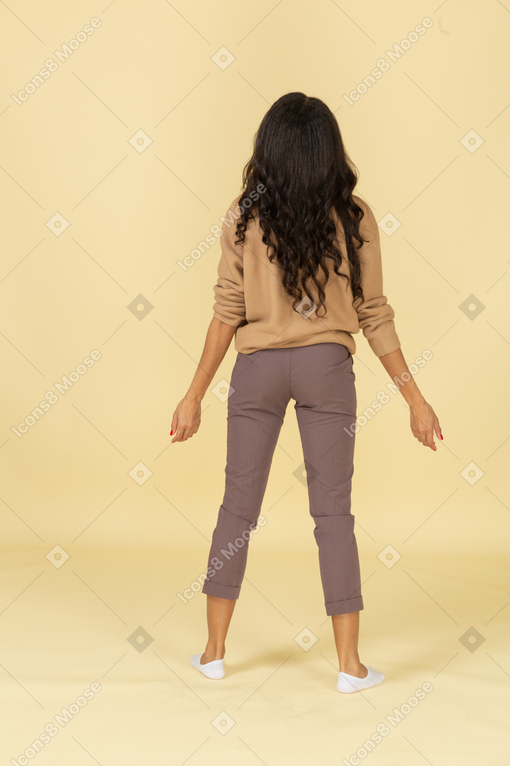 腕を広げて立っている浅黒い肌の若い女性の背面図