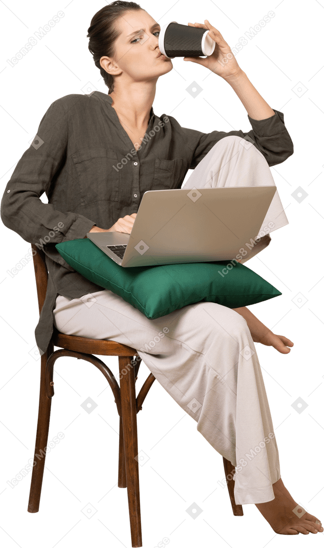 Vista frontale di una giovane donna seduta su una sedia che tiene in mano il suo laptop e beve caffè