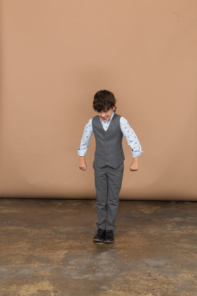 Vista frontal de un niño en traje mirando hacia abajo y extendiendo los brazos