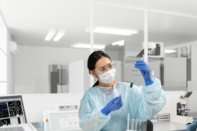 A female scientist wearing protective mask and glasses and holding a test tube