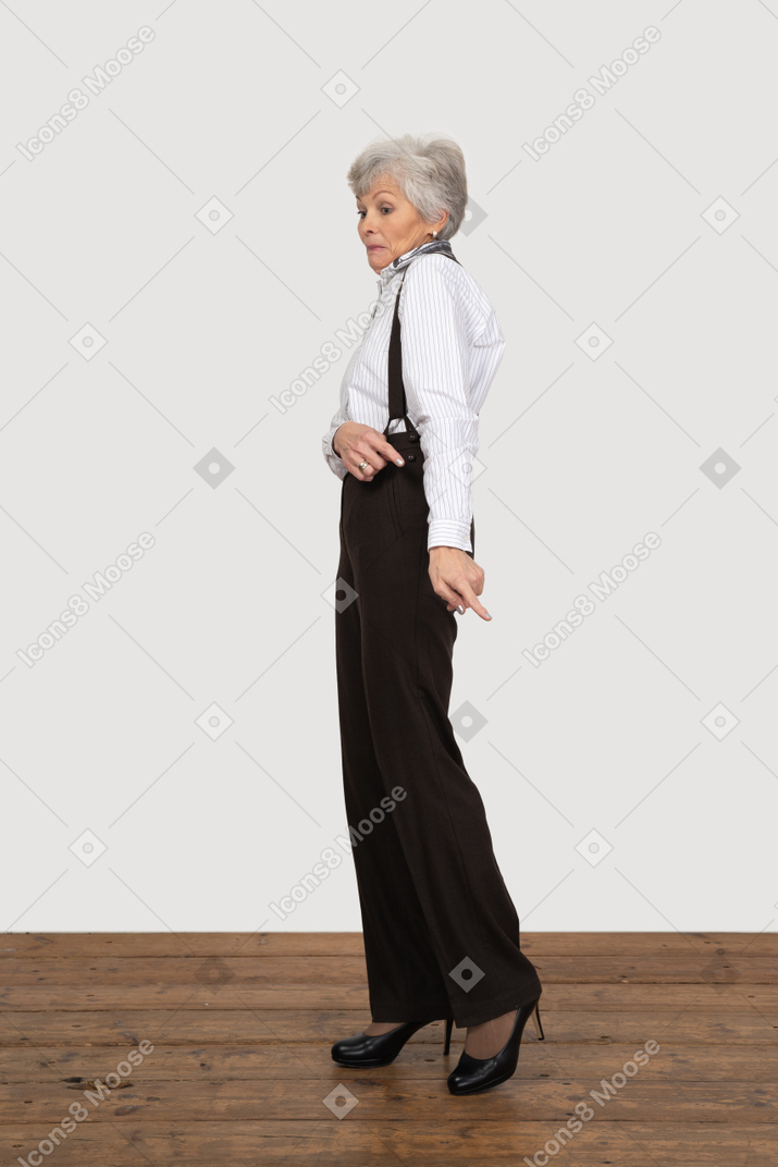 Side view of a funny perplexed old lady in office clothing pointing aside
