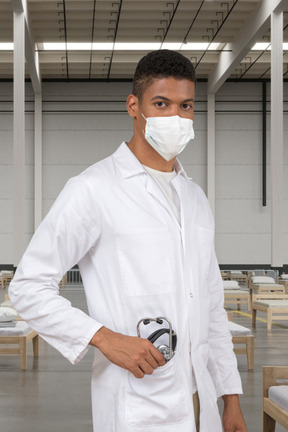 A doctor wearing a surgical mask and holding a stethoscope in his pocket