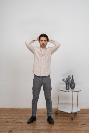 Vista frontal de um homem impressionado com roupas casuais em pé com as mãos atrás da cabeça