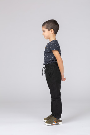 Vista lateral de un niño tímido en ropa casual de pie con las manos detrás de la espalda y mirando hacia abajo