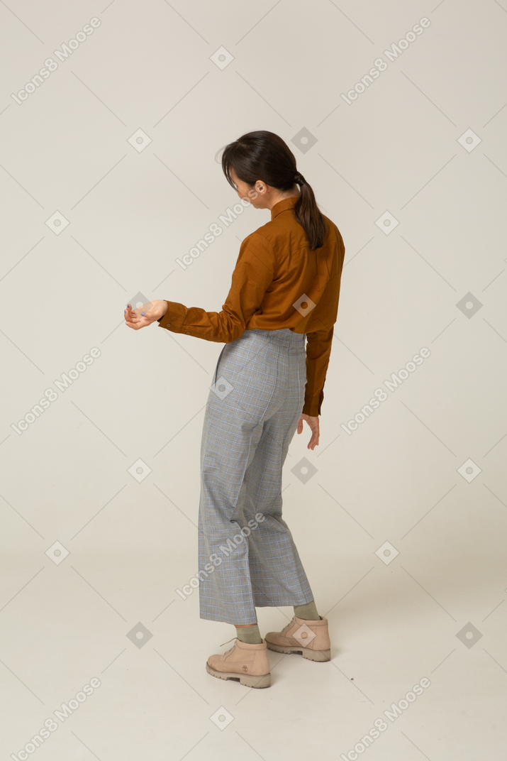Vue de trois quarts arrière d'une jeune femme asiatique en culotte et chemisier inclinant la tête et la main tendue
