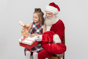 Garota garoto sentado nos joelhos do papai noel e segurando o brinquedo de pelúcia de veado