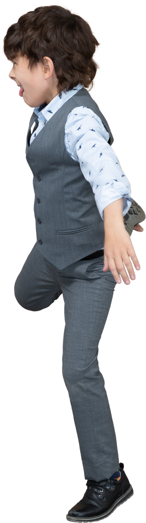 Vista laterale di un ragazzo in abito grigio in piedi su una gamba e che mostra la lingua