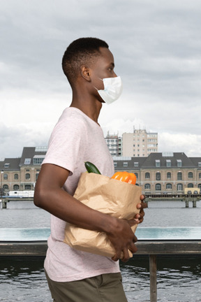 A man wearing a face mask holding a grocery bag
